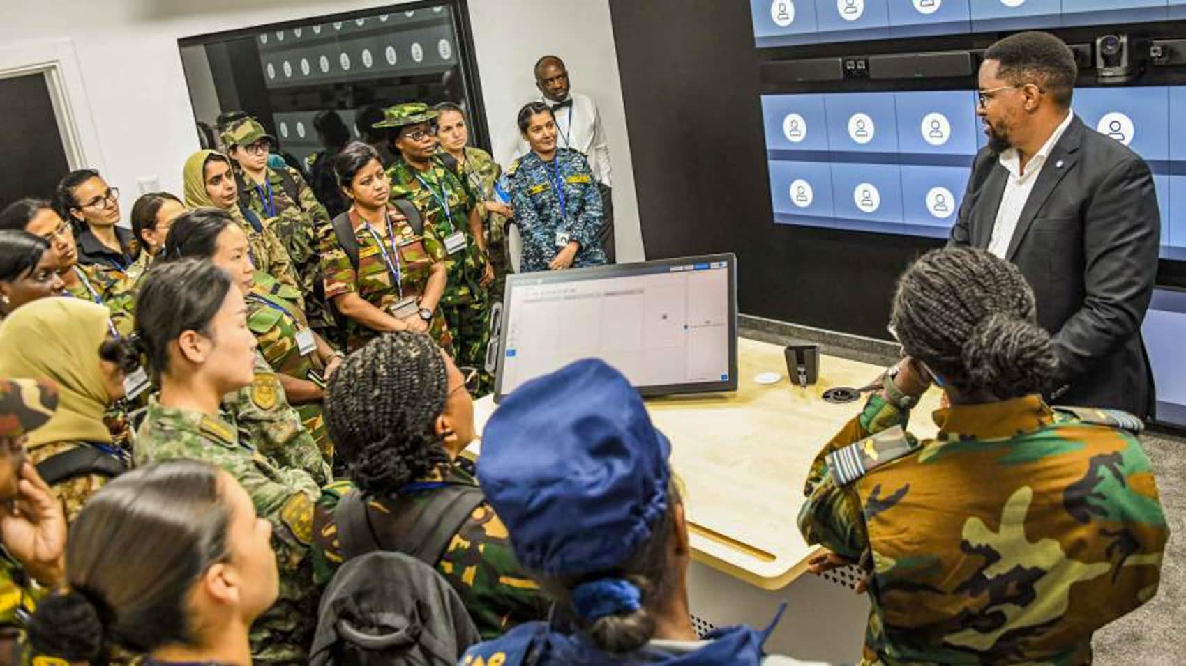 Women peacekeepers from several nations gather around a training screen with an instructor.