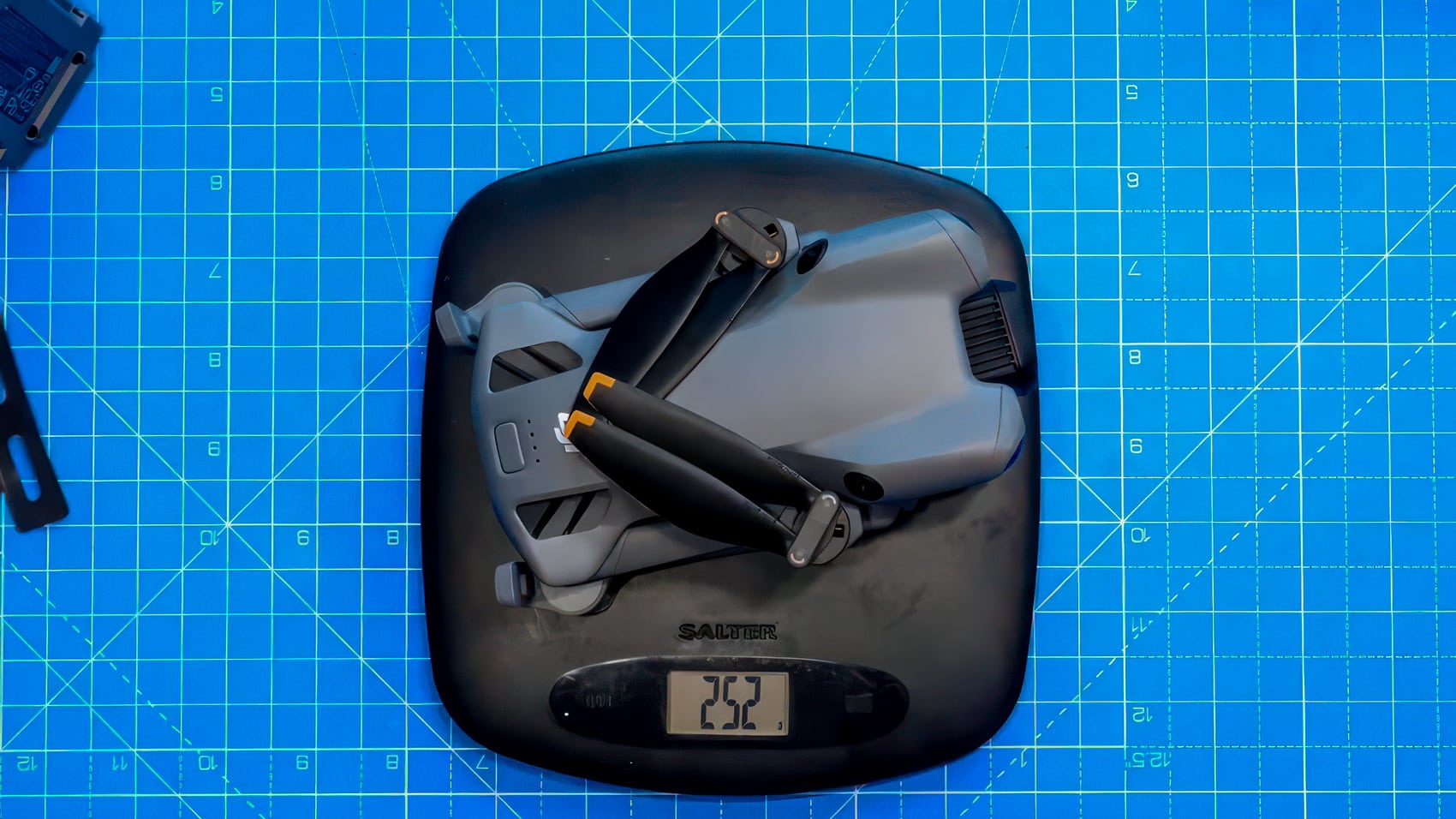 A folded Mini 5 Pro reads 252 grams on a Salter scale atop a blue cutting mat.