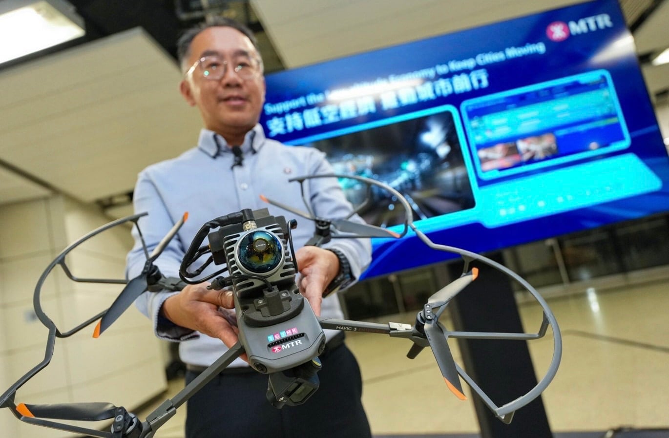 MTR engineer holds a caged inspection drone in front of a company display.