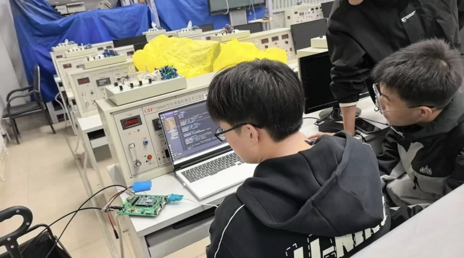 Chinese university students working on drone electronics at laboratory test benches.