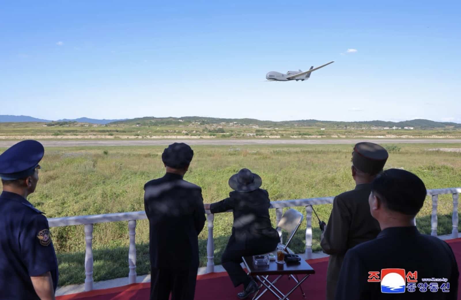 North Korean officials watch a large reconnaissance drone fly over marshland.