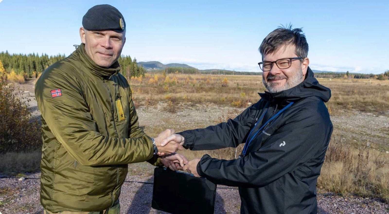 Uniformed officer and a civilian shake hands at an outdoor handover ceremony.