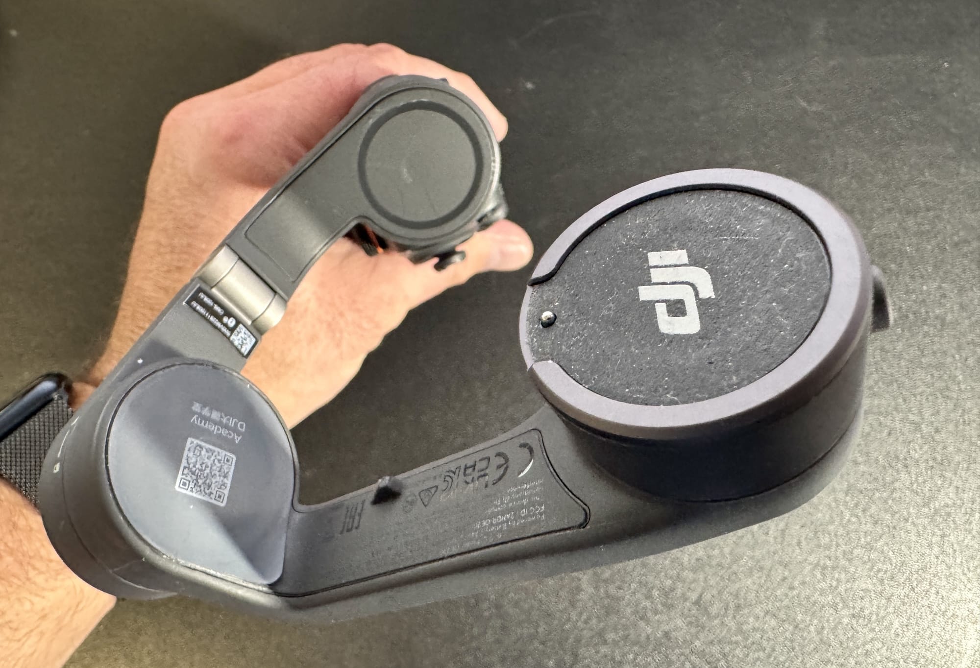 Hands holding an unreleased DJI handheld gimbal arm beside a round case.