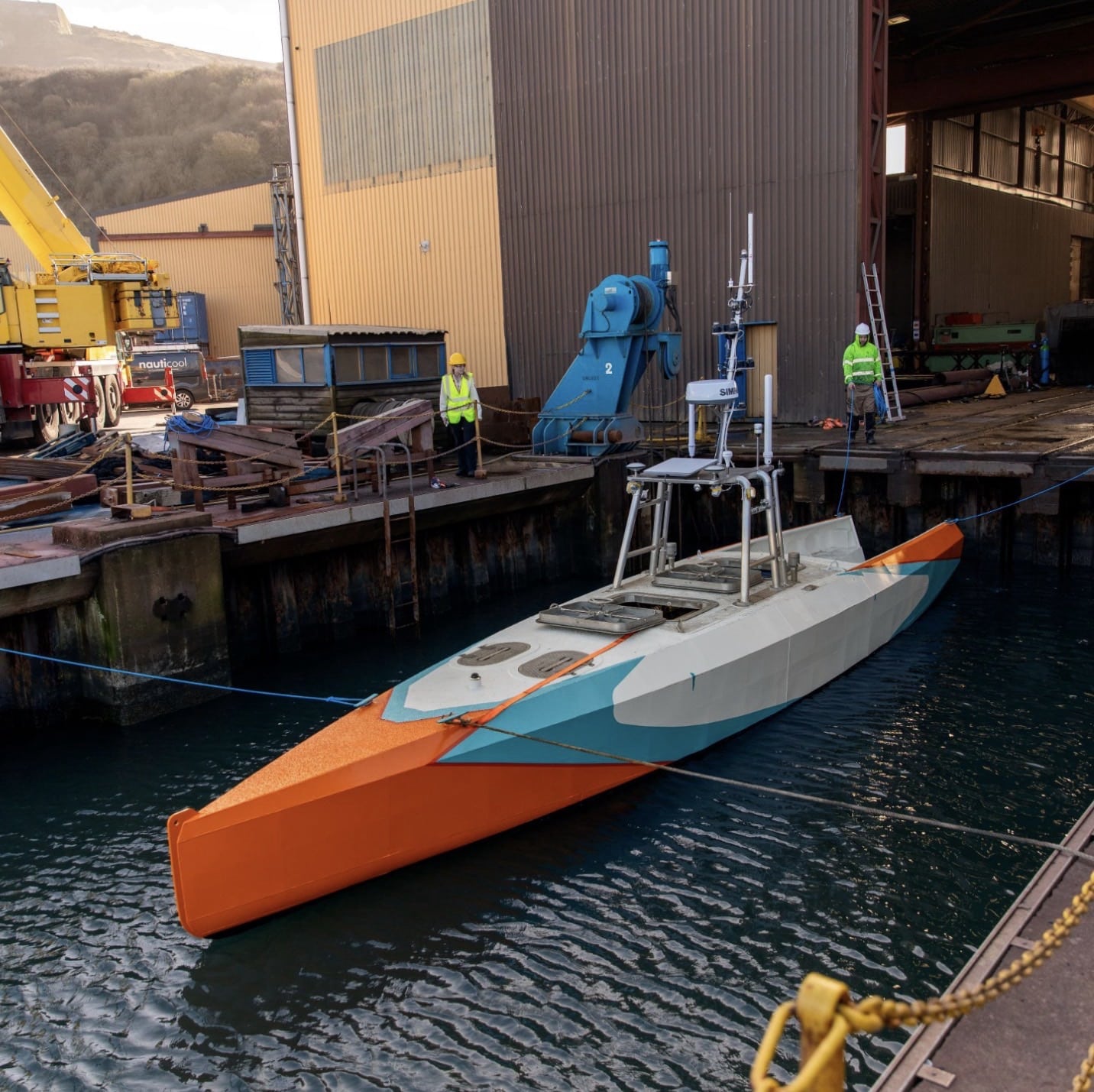 Uncrewed surface vessel moored alongside a dock at an industrial waterfront.