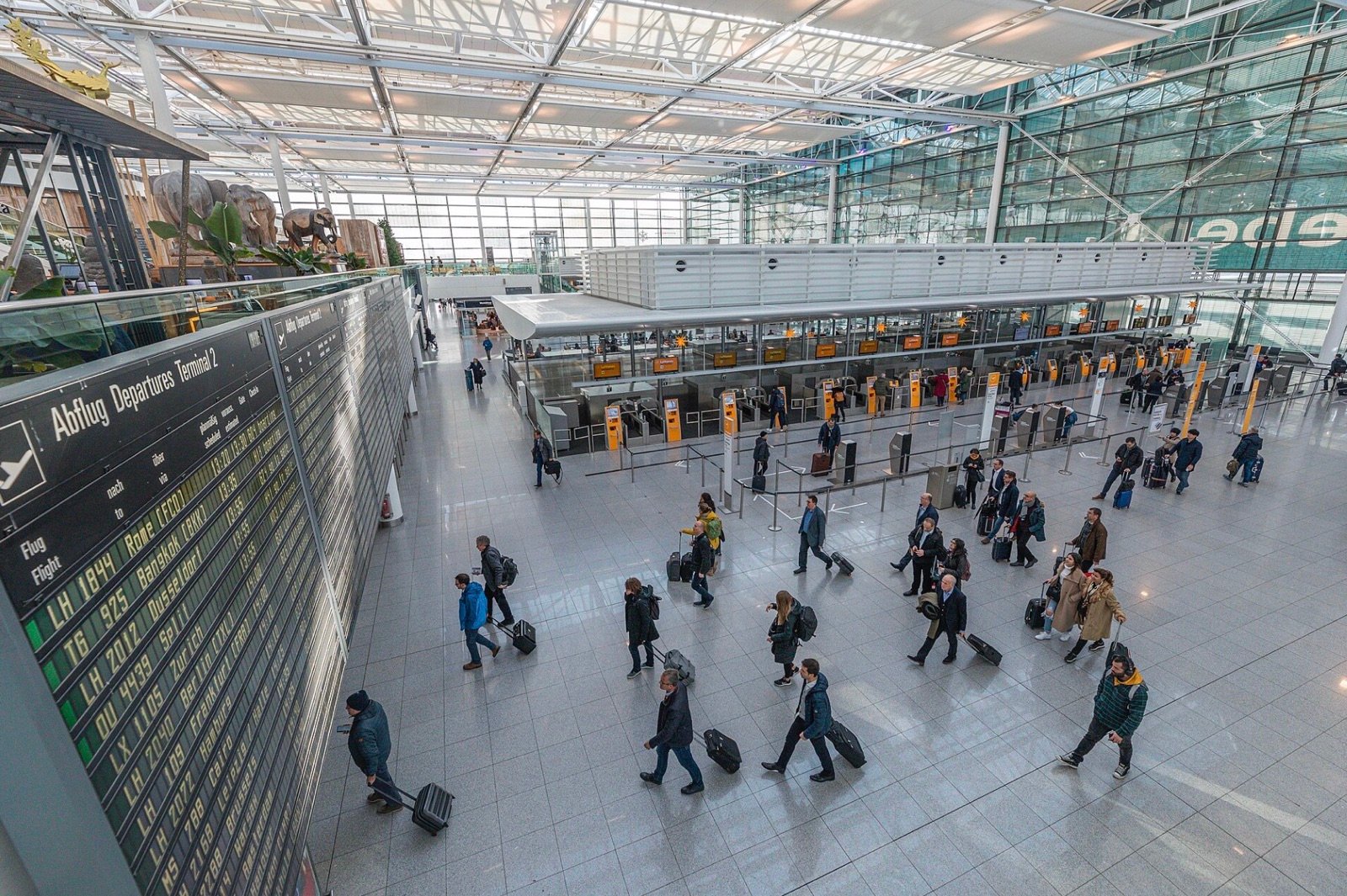 Travelers cross the check-in hall at Munich Airport beside a departures board.