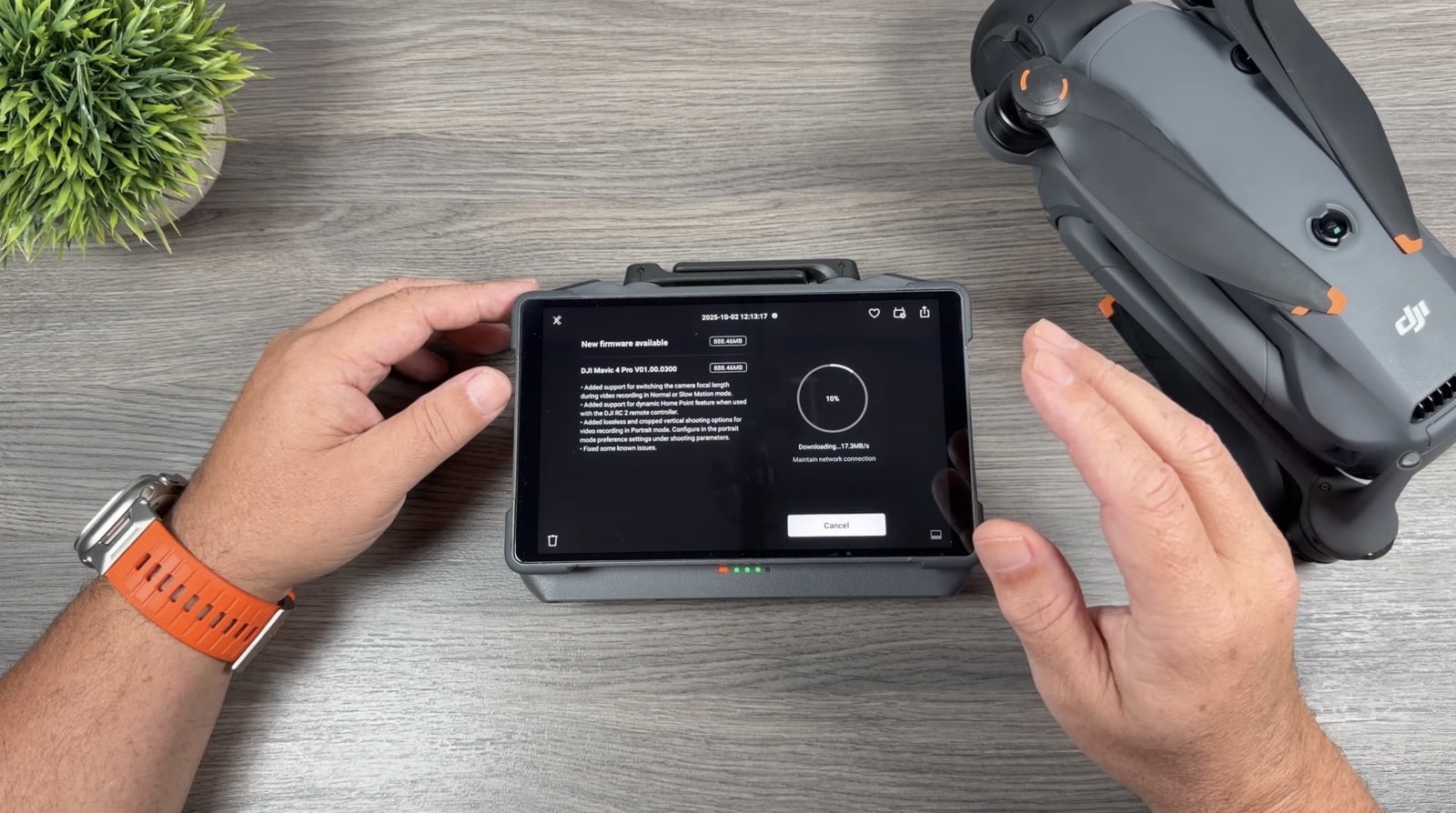 Hands using a DJI RC 2 showing a firmware update screen beside a folded Mavic.