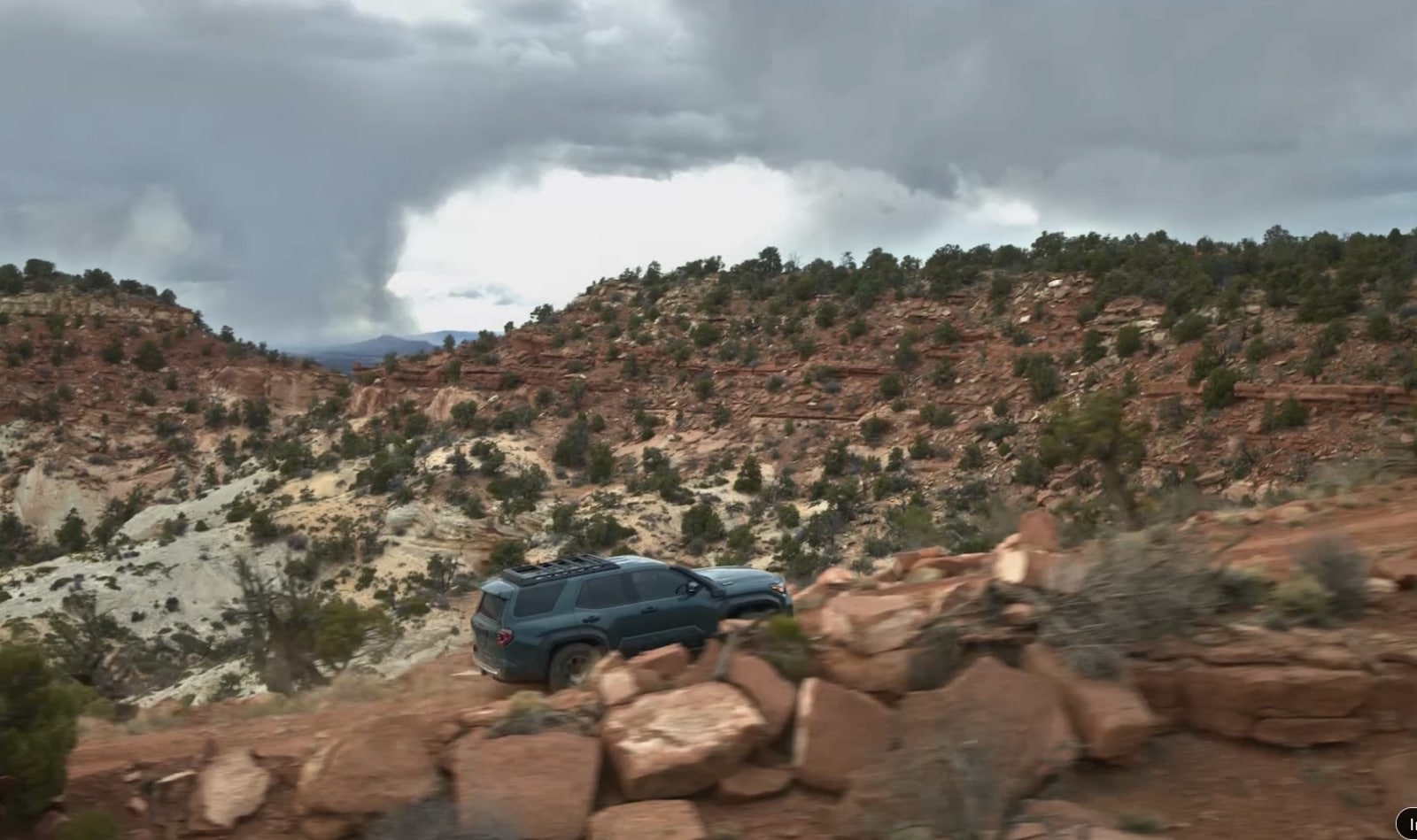 Toyota off-road SUV climbing rocky red desert terrain under a stormy sky.