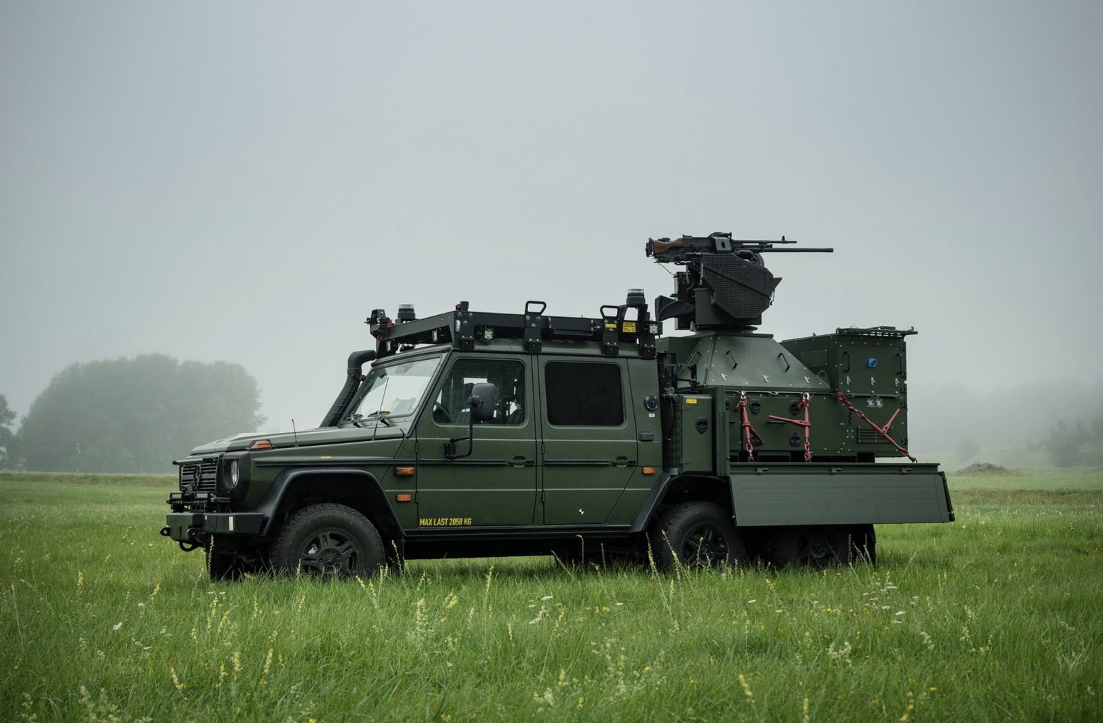 Military light vehicle fitted with a remote weapon turret in a misty field.