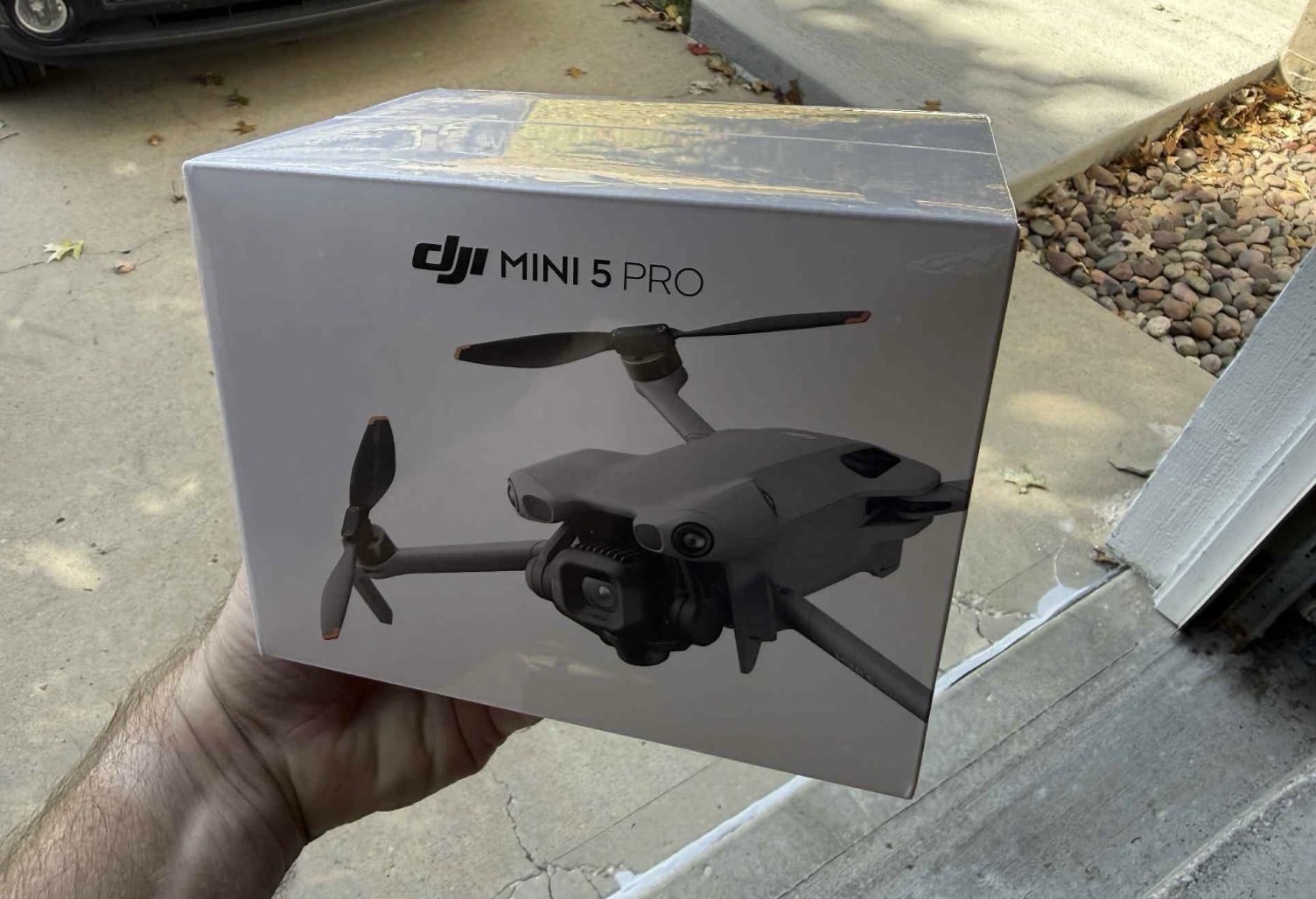 Hand holding the retail box of the DJI Mini 5 Pro on a doorstep.