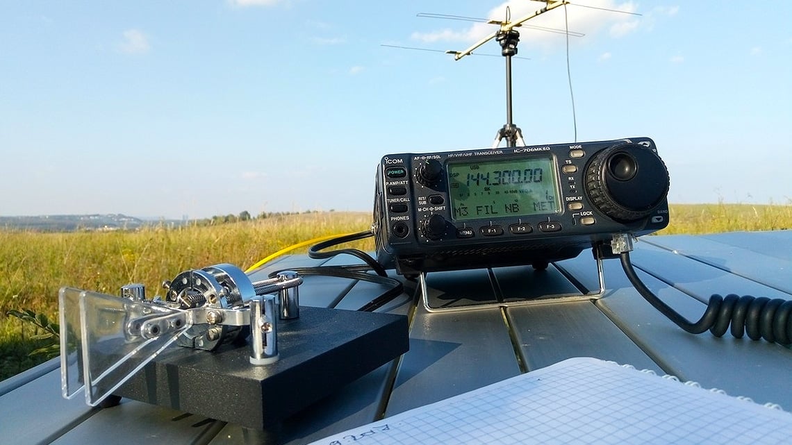 Mobile ham radio transceiver and whip antenna set up beside open farmland.