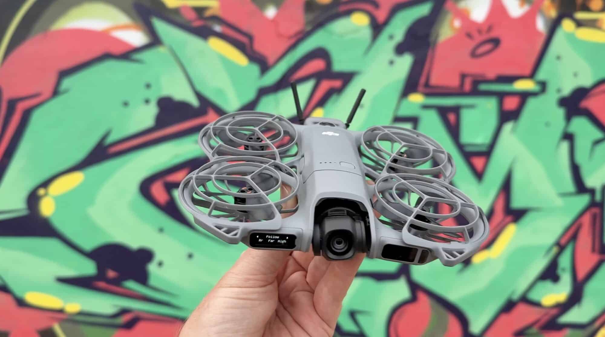 Hand holds the DJI Neo 2 in front of a brightly painted graffiti wall.