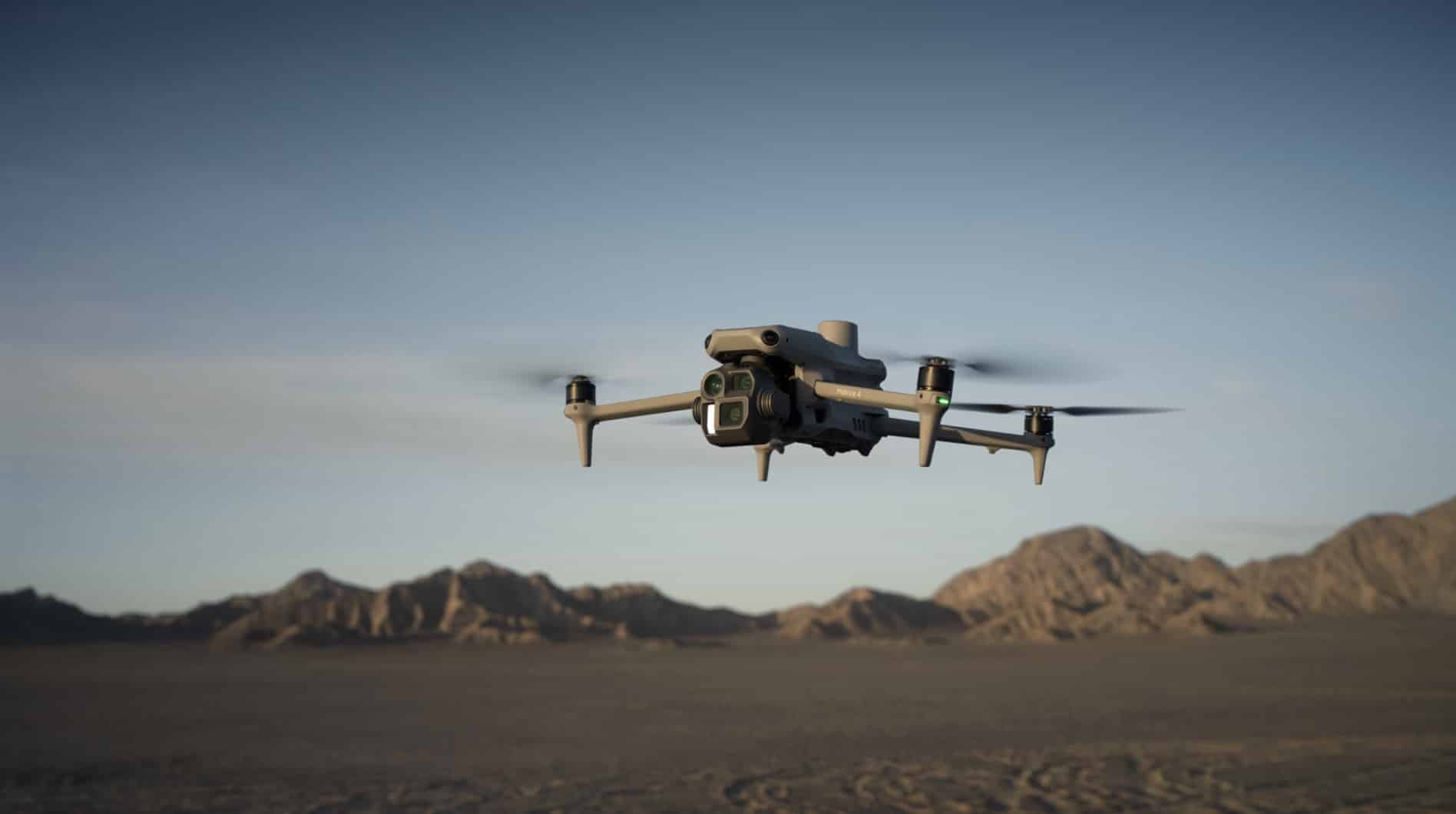 Quadcopter hovering low over dark desert flats and distant ridges.