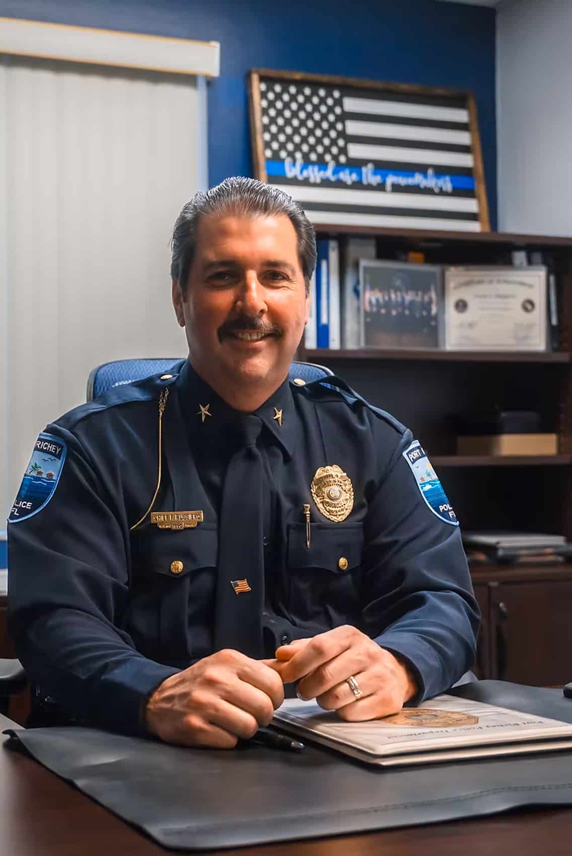 Port Richey Police Chief Frank Ruggiero seated at his desk in uniform.
