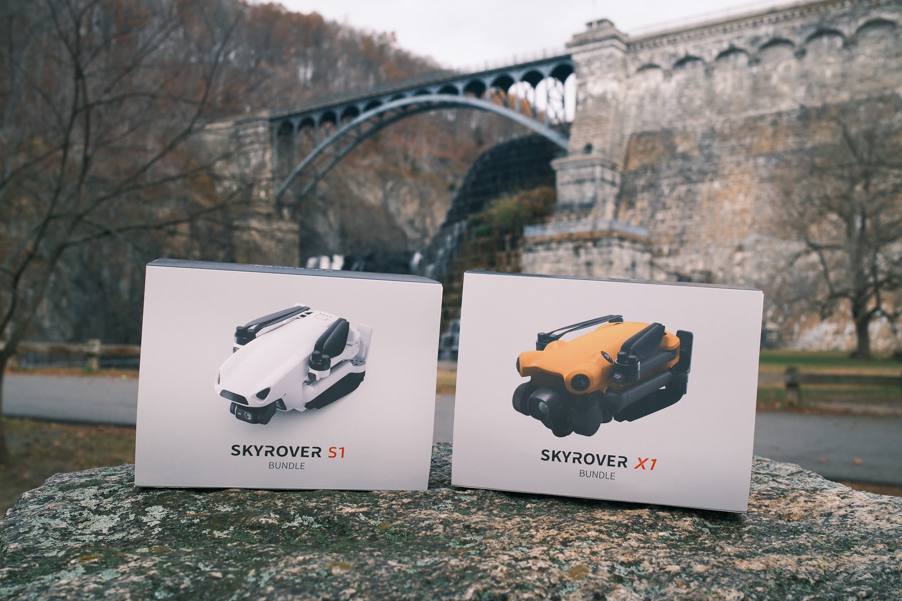 Skyrover S1 and X1 retail boxes propped on a rock before a stone bridge.