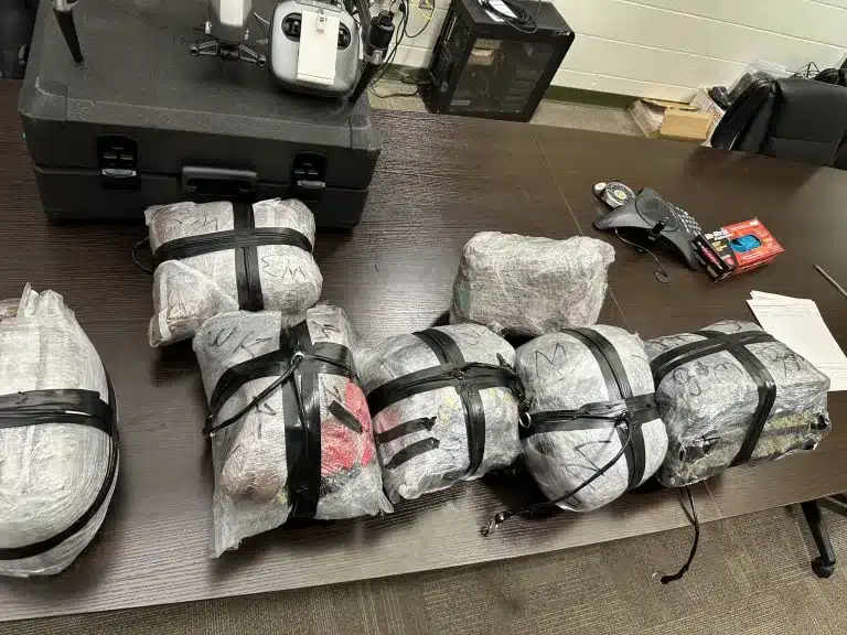 Bundles of seized contraband strapped in plastic on a table beside a drone and controller.