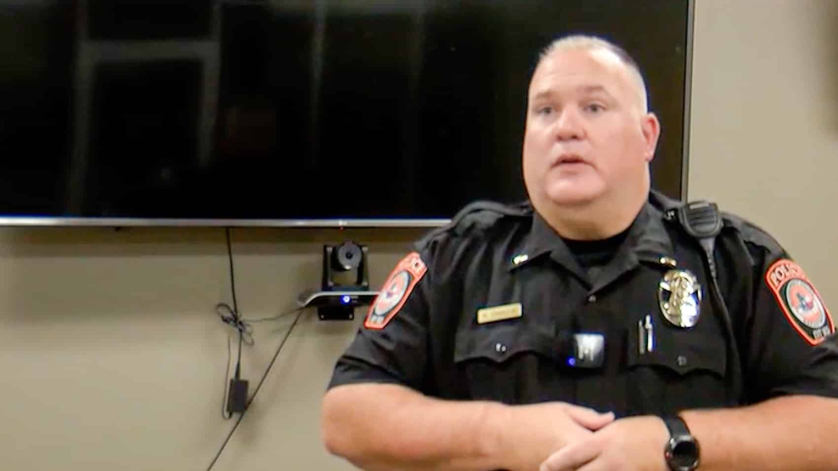 Police officer in uniform speaks to reporters inside a briefing room.