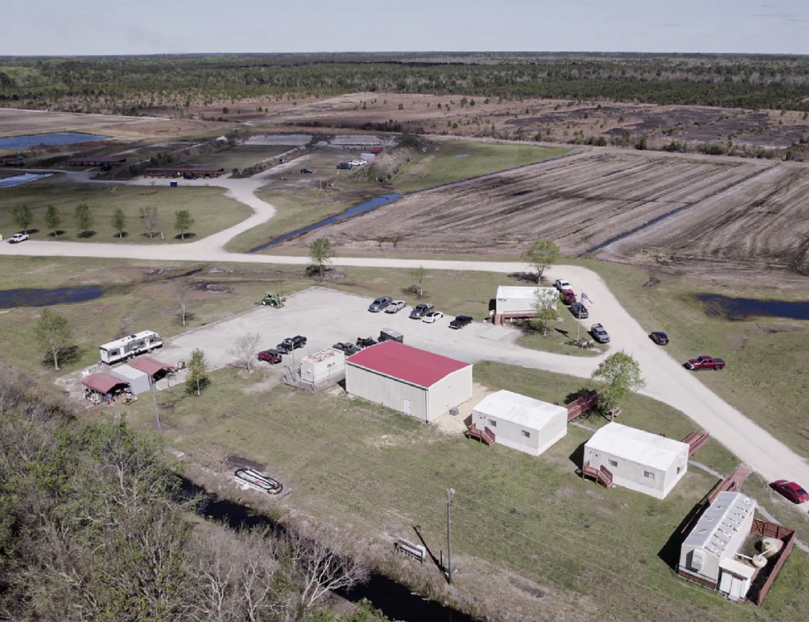 Aerial view of a rural drone test range with sheds, trailers, and parked vehicles.
