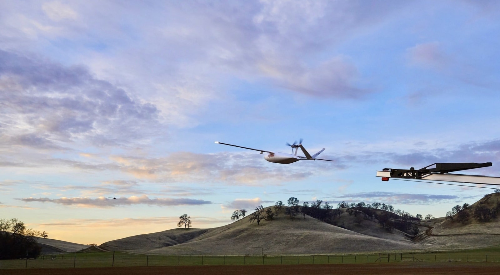 Two Zipline delivery aircraft cruise above rolling green hills at dusk.