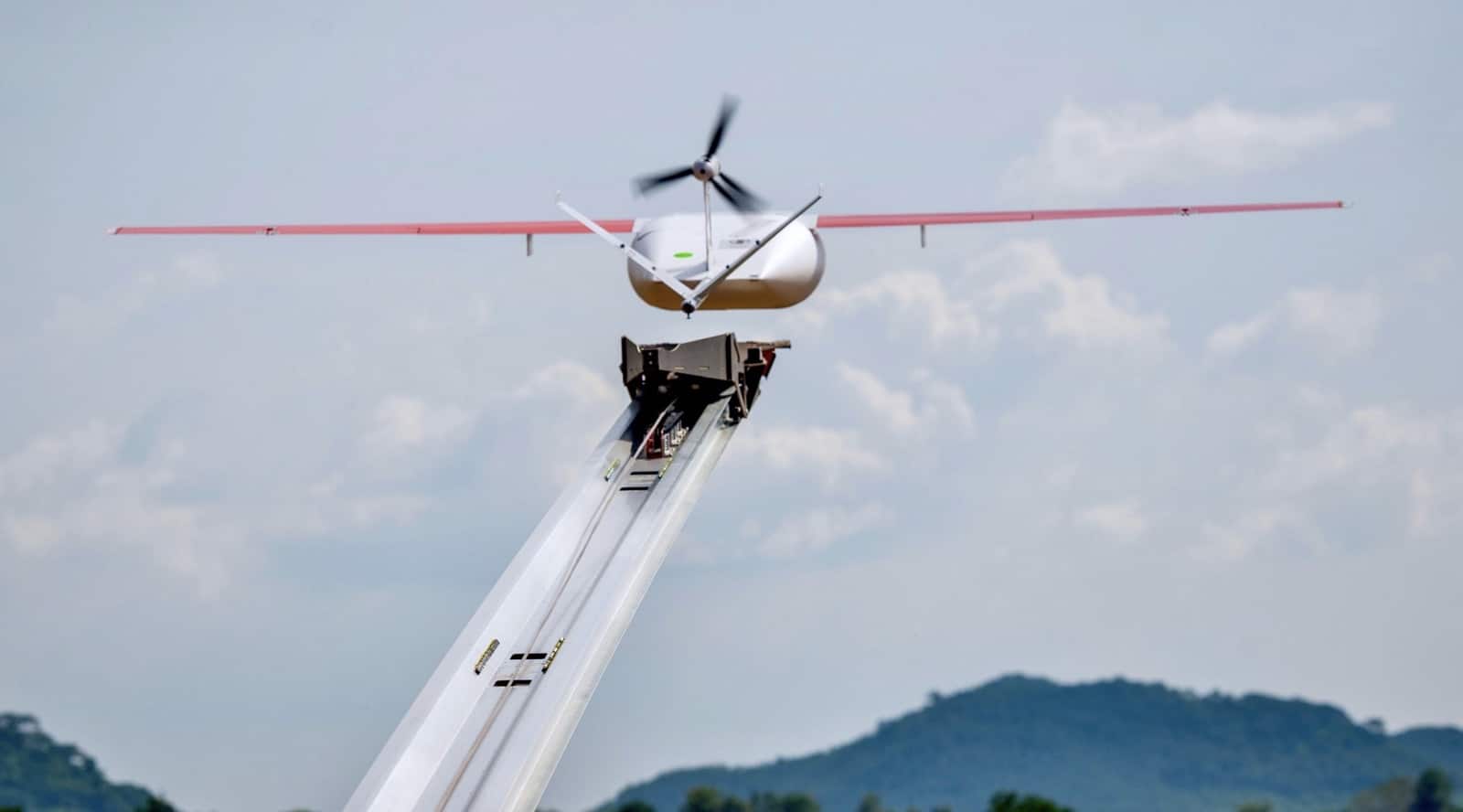 A Zipline fixed-wing delivery drone sits on its catapult launcher against cloudy hills.