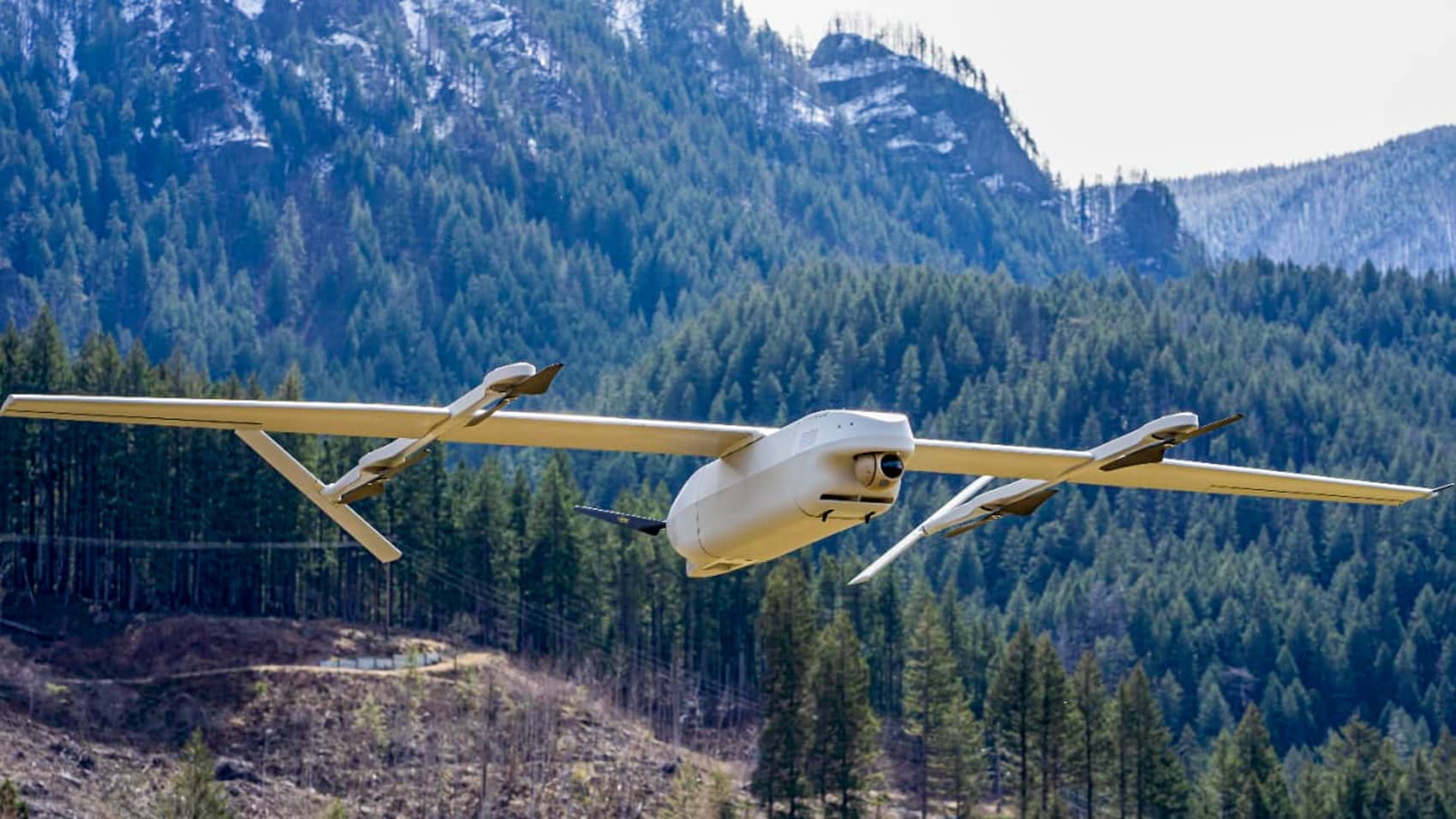 Heven AeroTech fixed-wing drone cruising above a forested mountain valley.