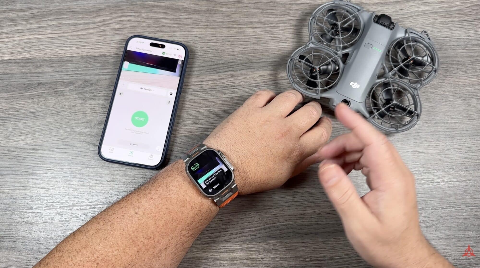 Hands wearing an Apple Watch beside a DJI Neo 2 and a phone.