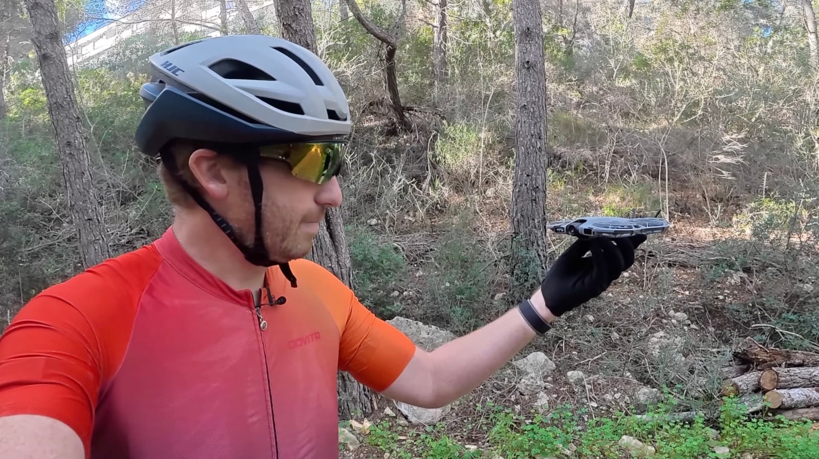 Cyclist in an orange jersey holding the Neo 2 flat on his gloved palm on a trail.