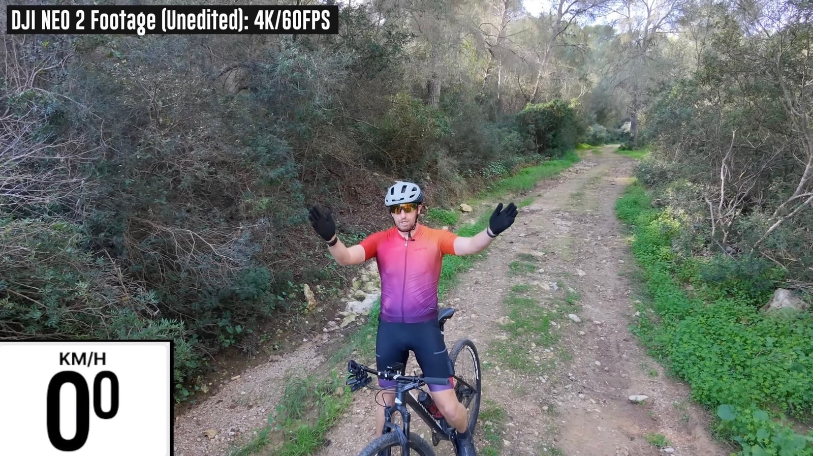 Unedited 4K Neo 2 frame of a cyclist stopped arms-out on a dirt trail.