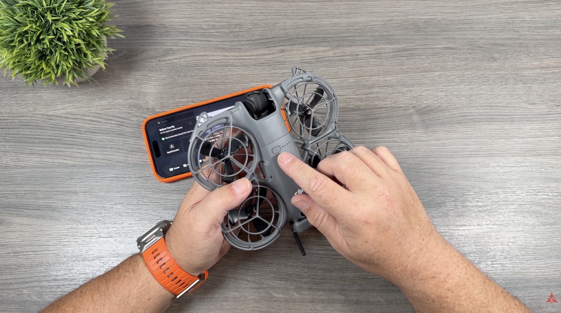Hands hold a DJI Neo 2 with propeller guards beside a smartphone.