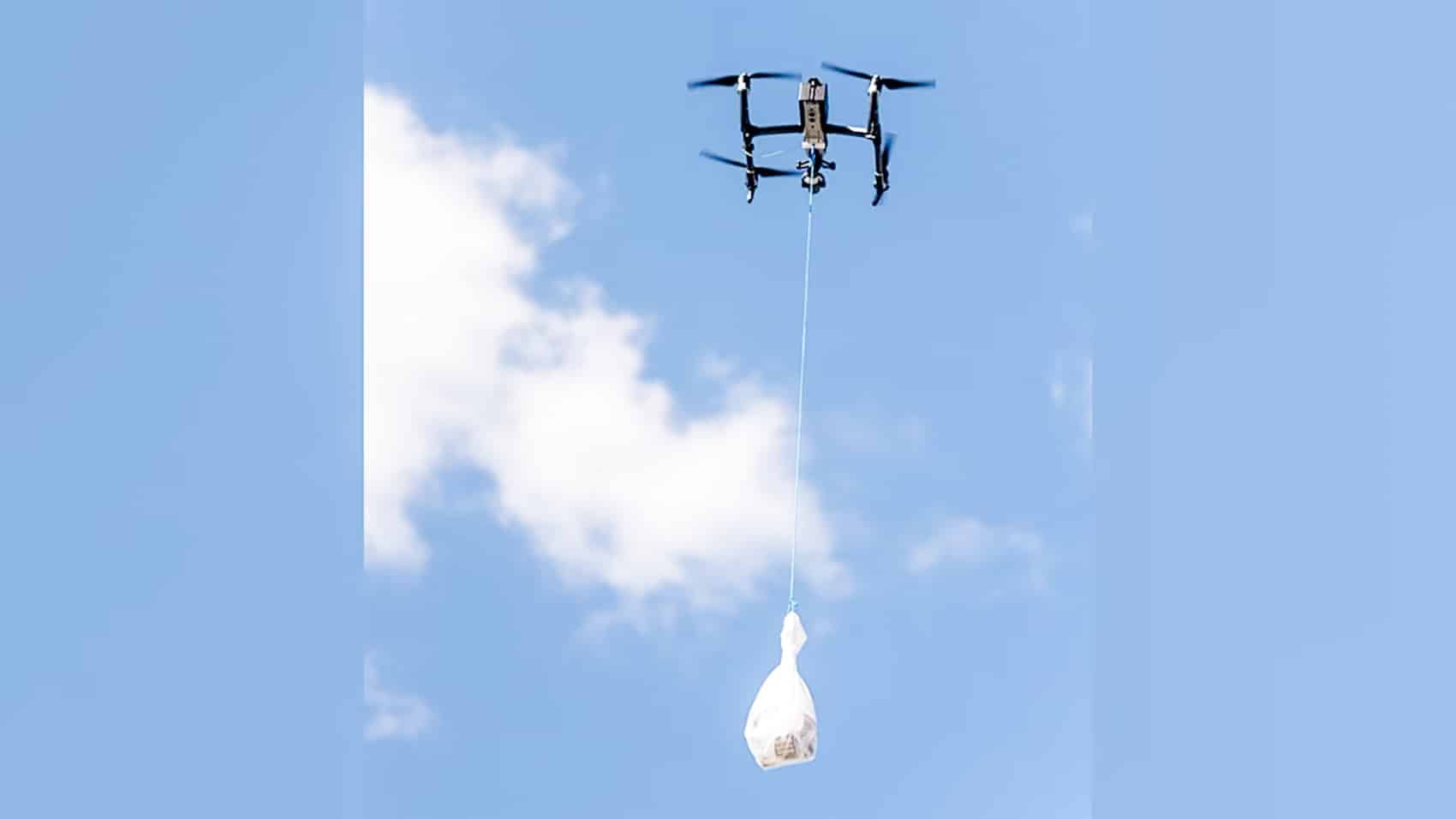Drone in a blue sky lowering a white smuggling bundle on a line.