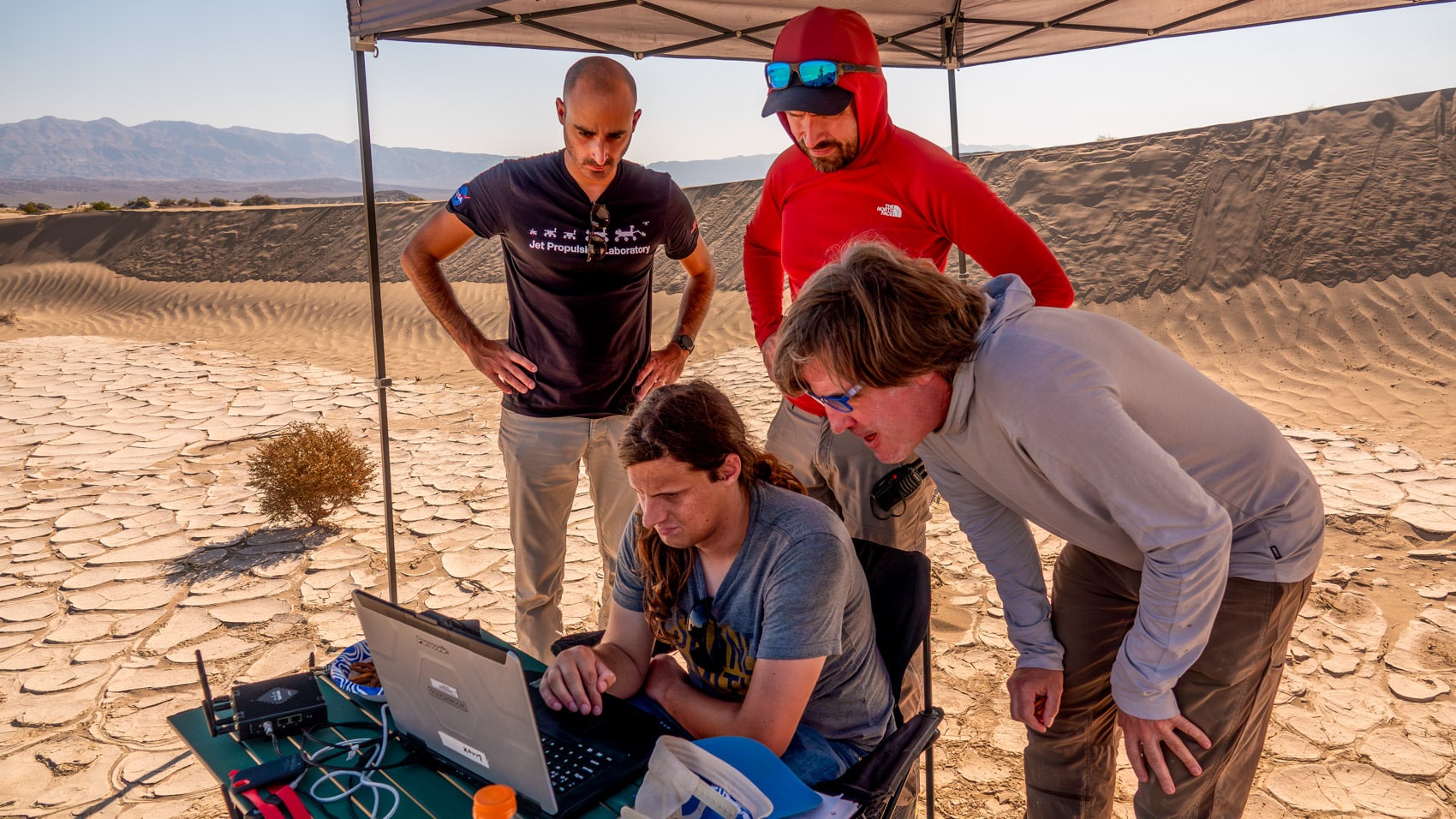 JPL researchers monitoring drone tests from a pop-up shade tent in the desert.