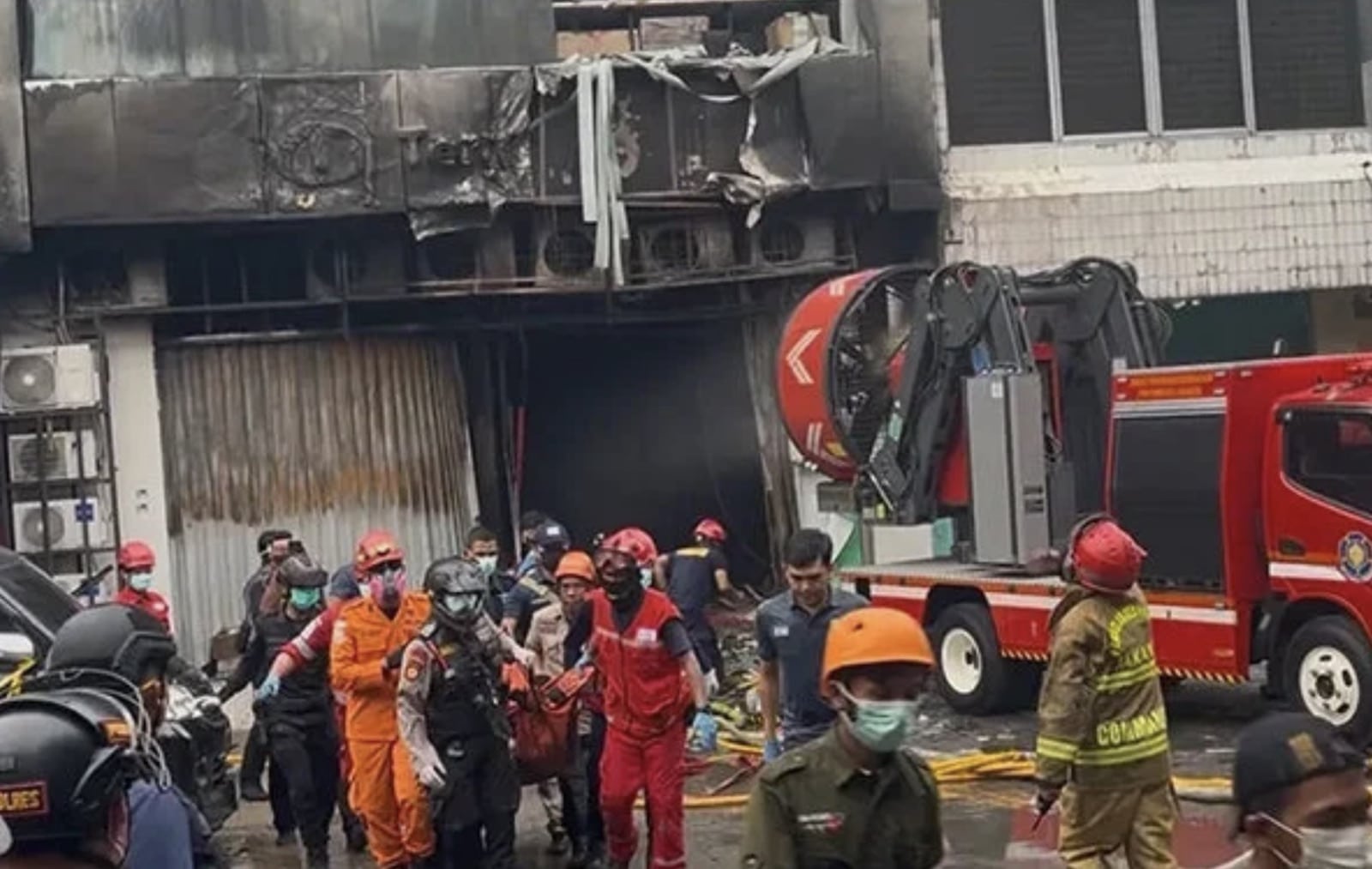 Rescue workers carry a stretcher past the fire-blackened Jakarta office block as fire trucks stand by.