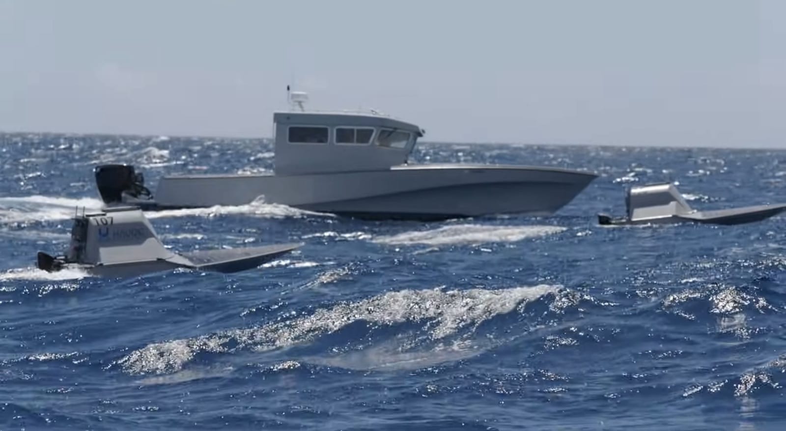 Autonomous drone boats running alongside a larger vessel in choppy open water.