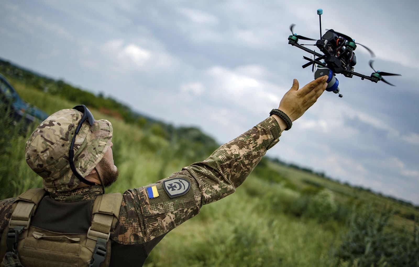 A Ukrainian soldier reaching up to catch an FPV drone above a field.