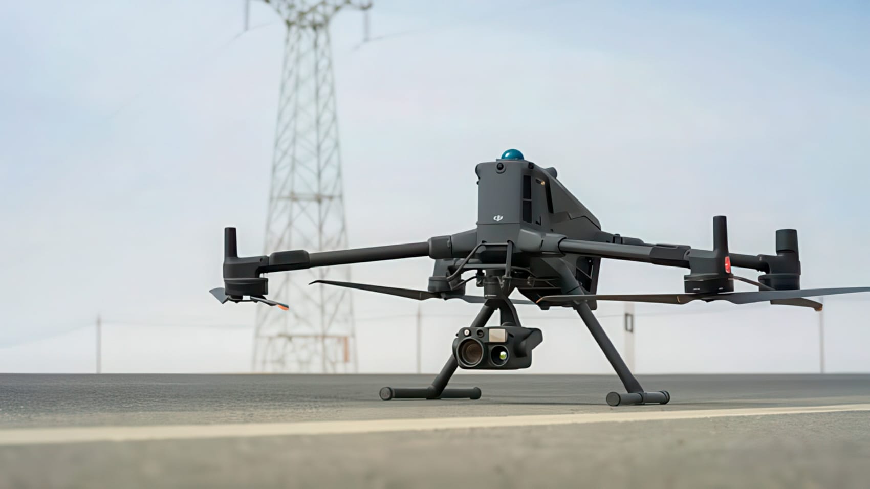 Large DJI Matrice quadcopter parked on a road with a transmission tower behind.