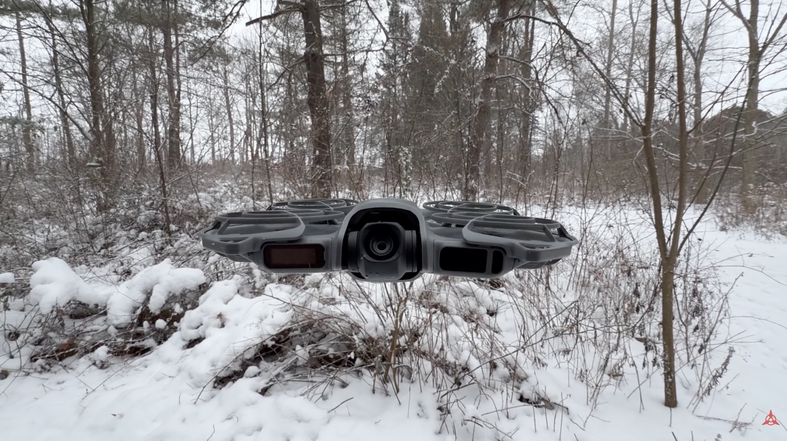 A DJI Neo 2 hovering above a snowy woodland clearing in winter.