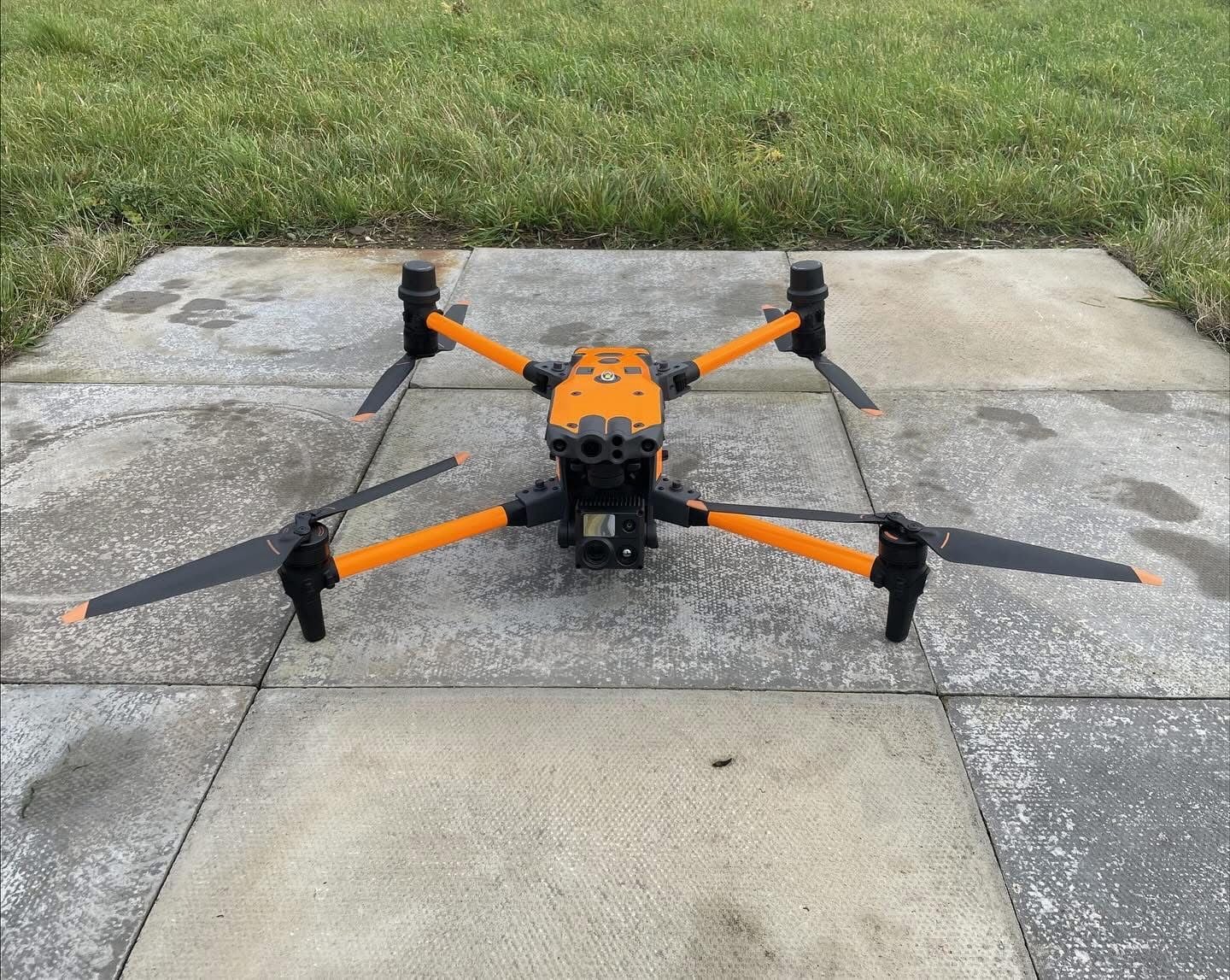 Orange-wrapped DJI Matrice 30 sitting on a concrete pad beside grass.