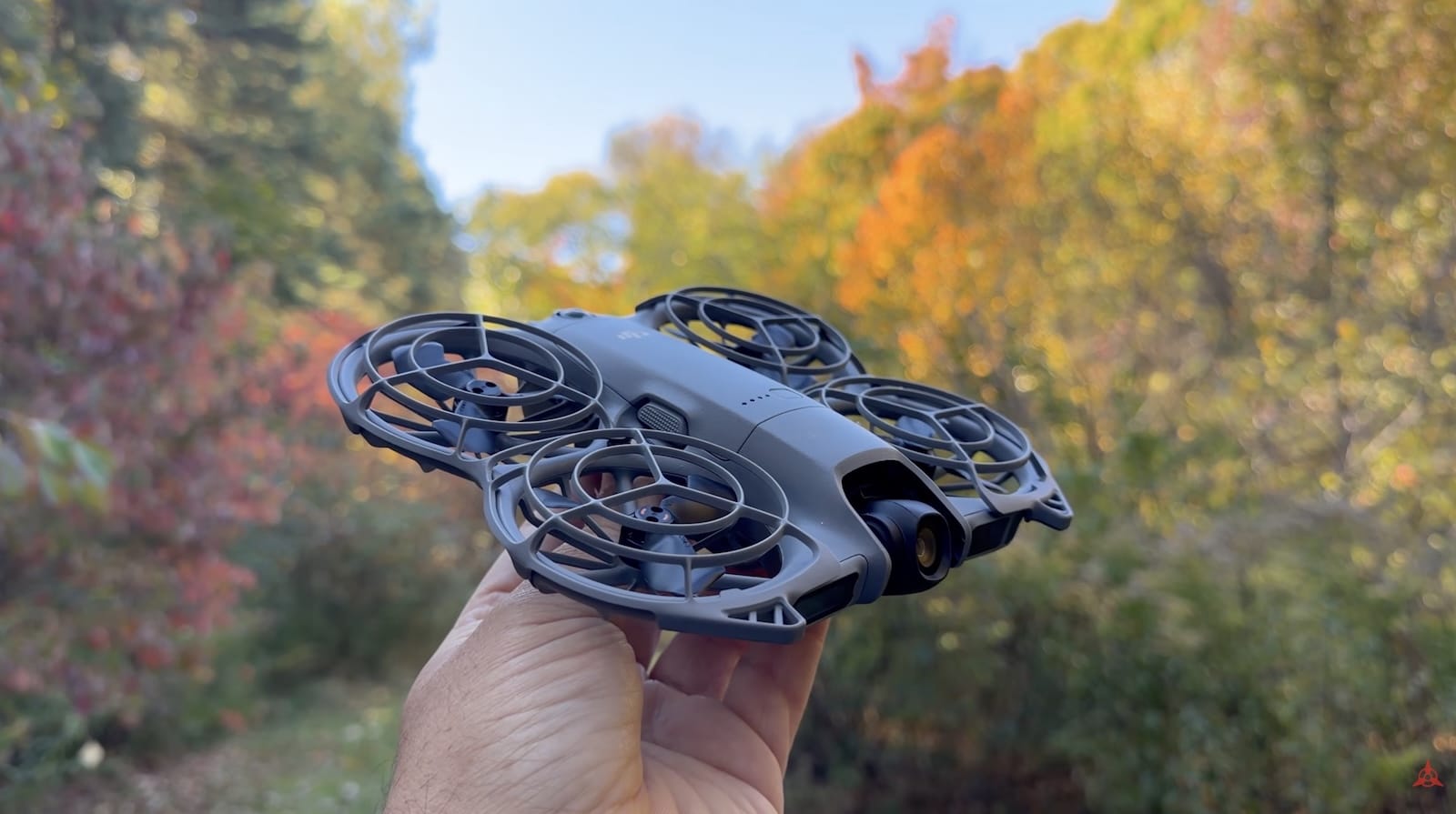 Hand holds the DJI Neo 2 with autumn foliage filling the background.