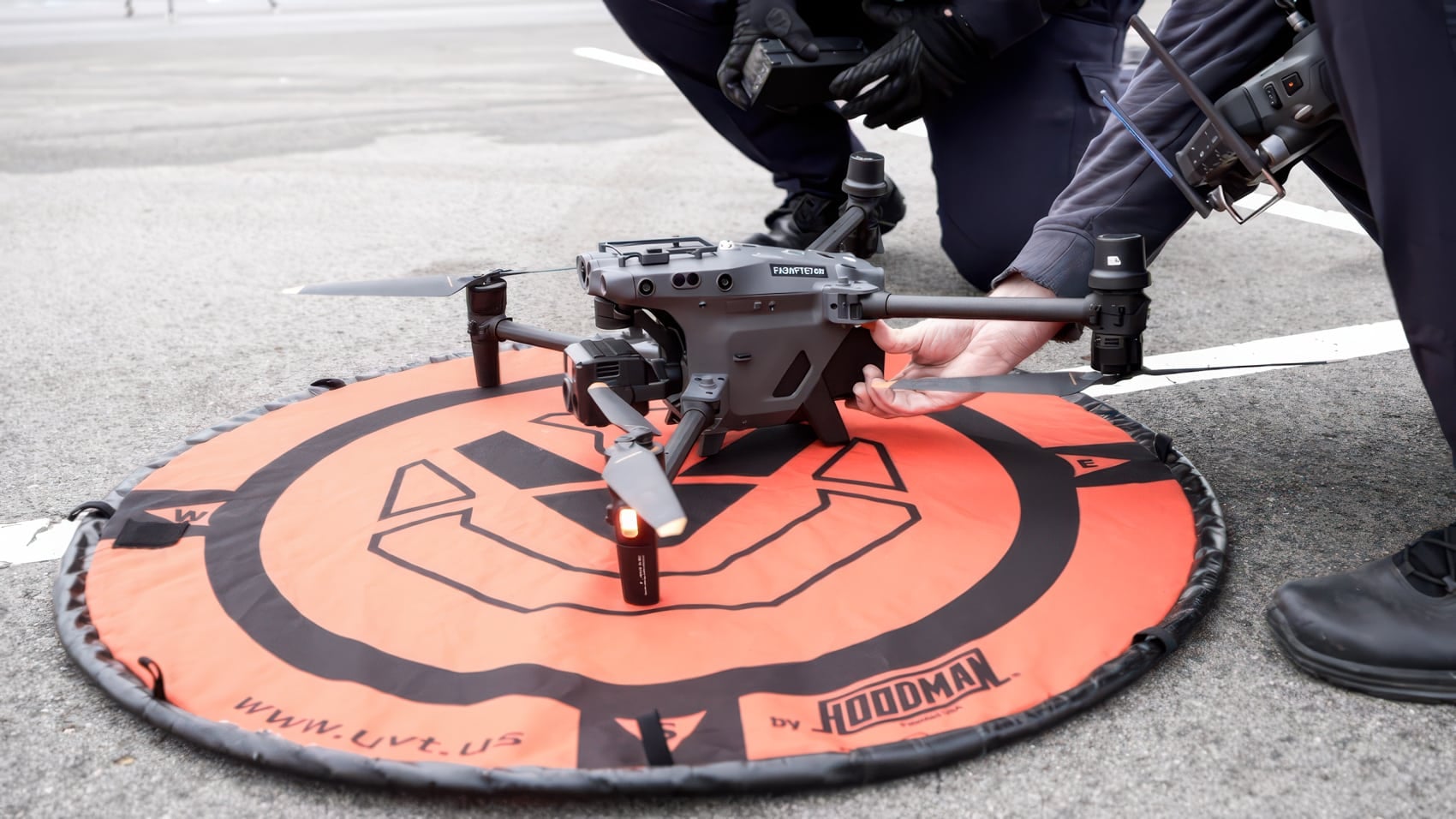 Officers set up a grey quadcopter on an orange landing pad in a parking lot.