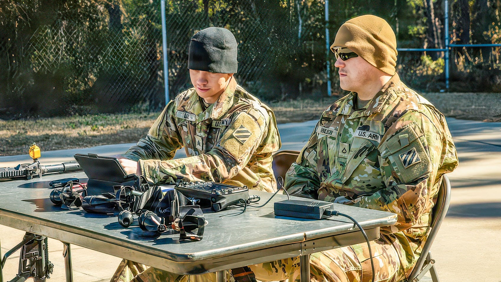 Two US Army soldiers assembling drone components at an outdoor field table.
