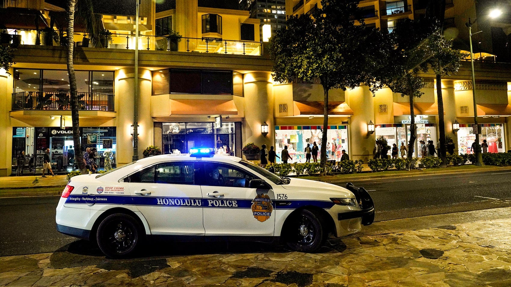 A Honolulu Police cruiser parked along a lit Waikiki street at night.
