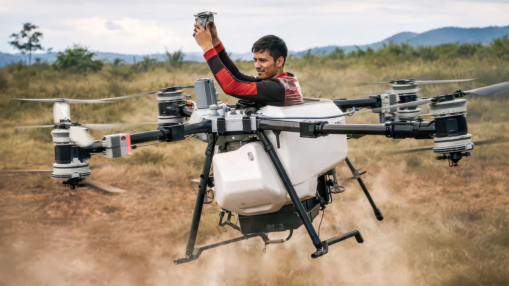 Man rides on a large agricultural spraying drone hovering above a dirt field.