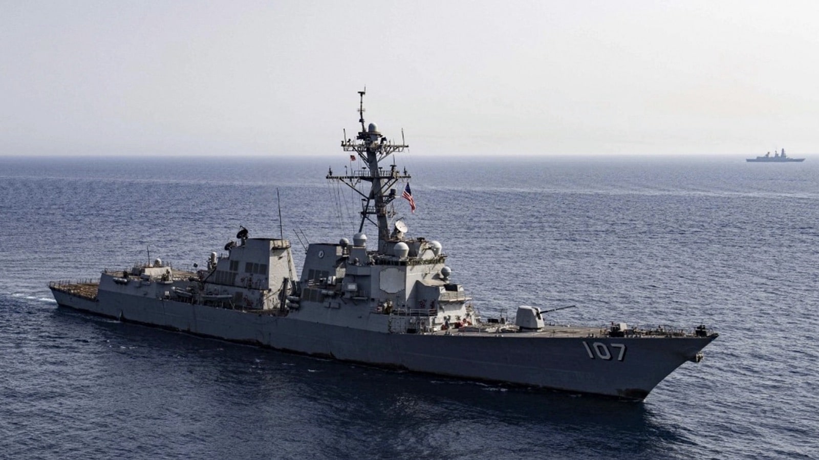 An Arleigh Burke class destroyer numbered 107 steams across a flat grey sea.