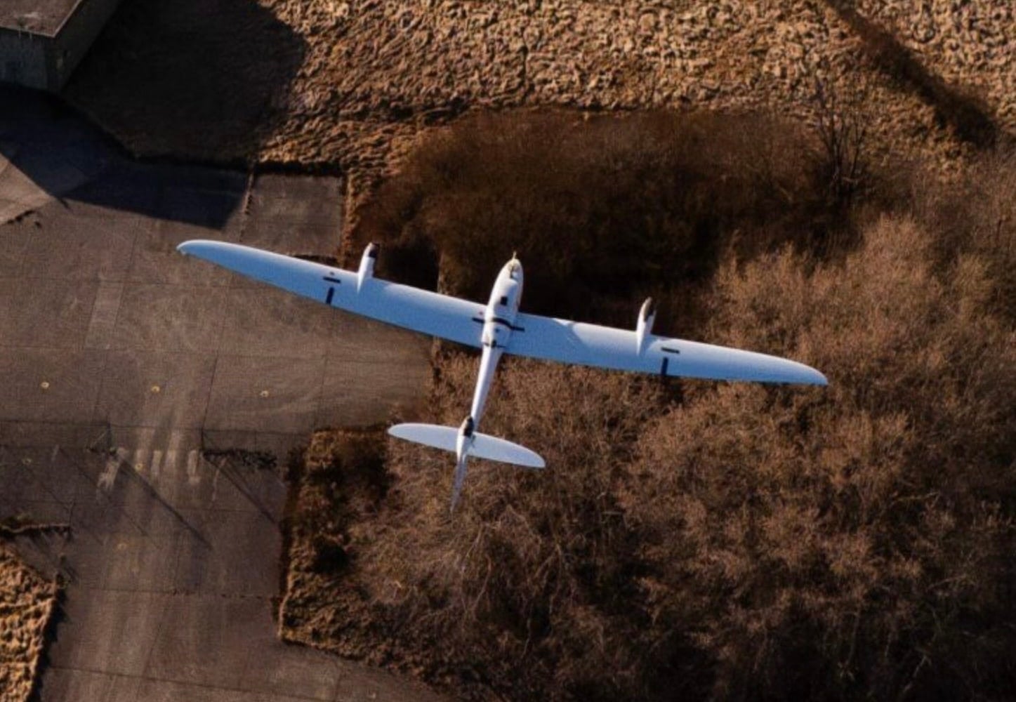Quantum Systems fixed-wing drone flies low over ploughed farmland.