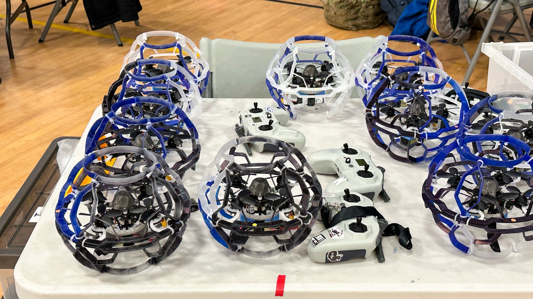 Students piloting glowing caged drones inside the netted drone soccer arena.