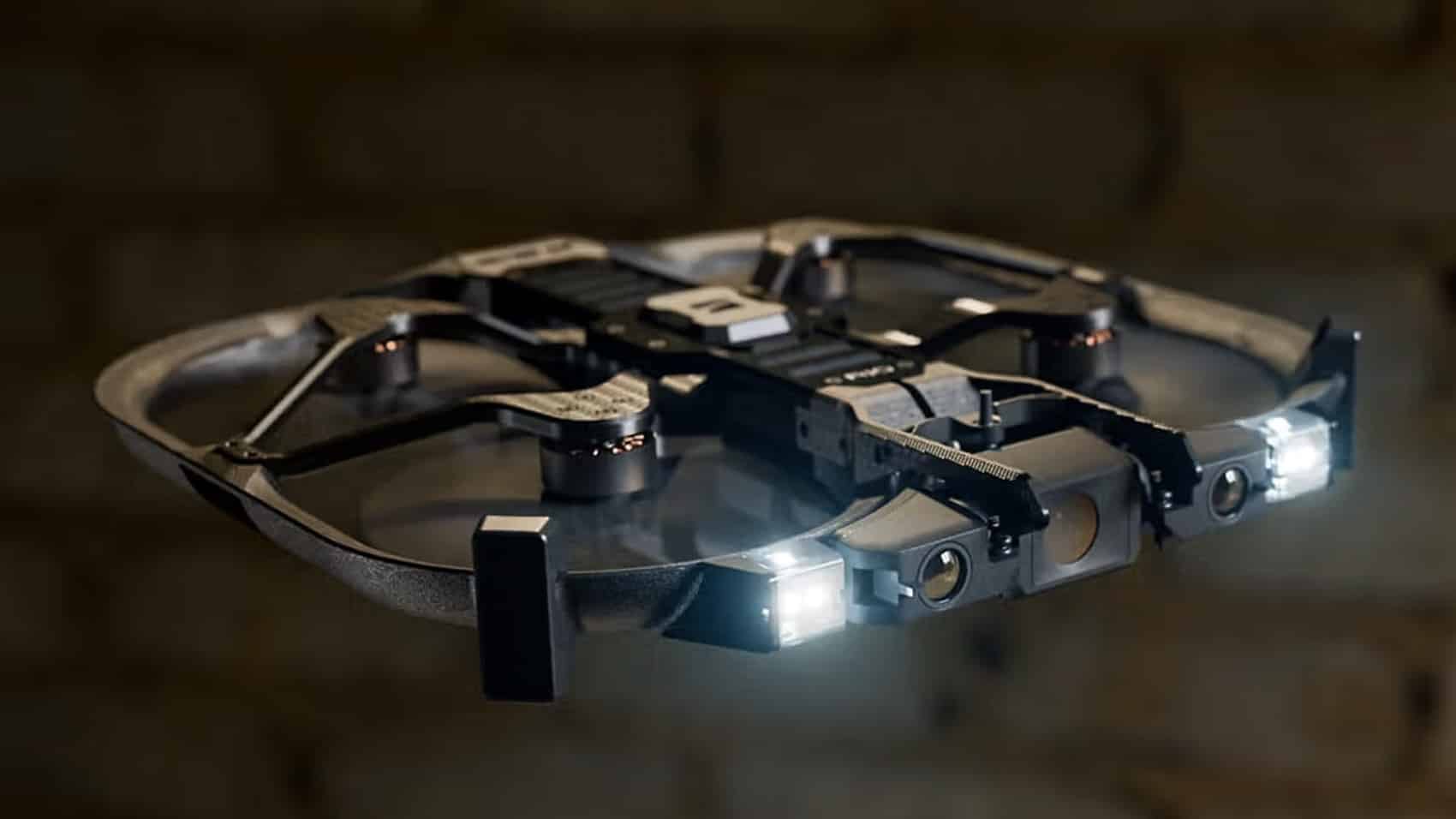A Skydio R10 with prop guards flying beside a brick wall indoors.