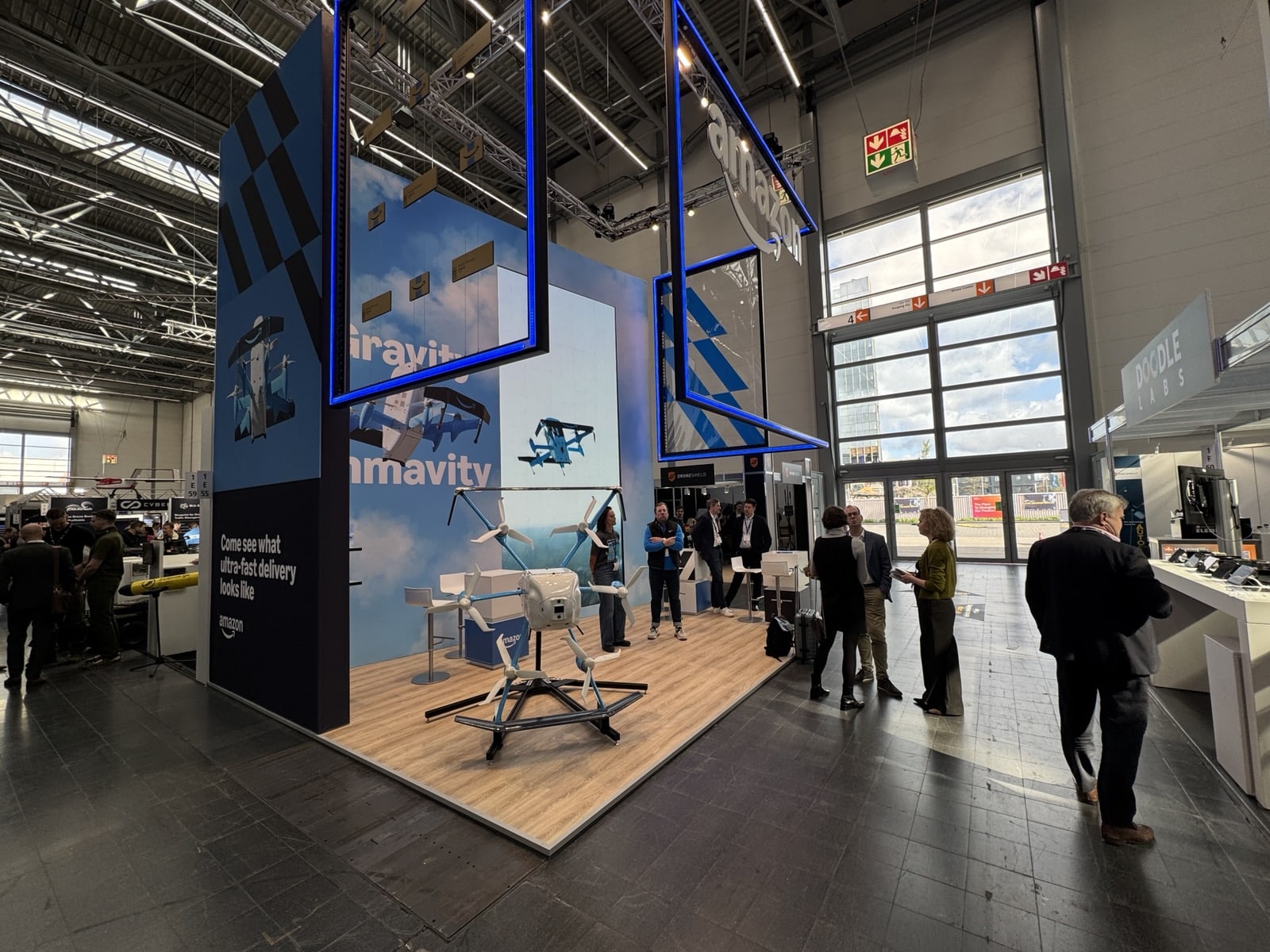 Visitors walk past the blue trade-show stand with a drone on its plinth.