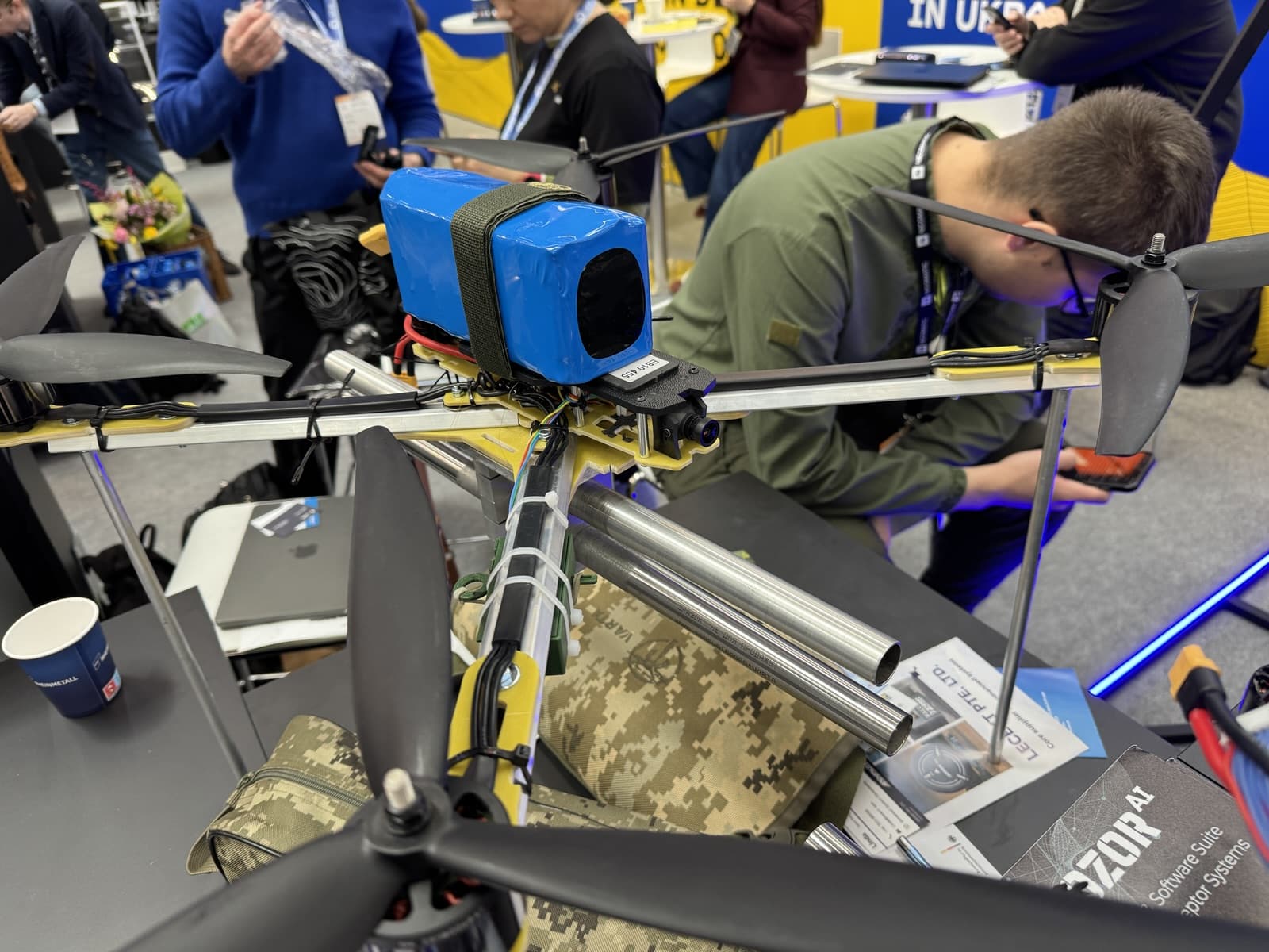 Exhibitor adjusting a large multirotor with a blue payload at a defense trade show.