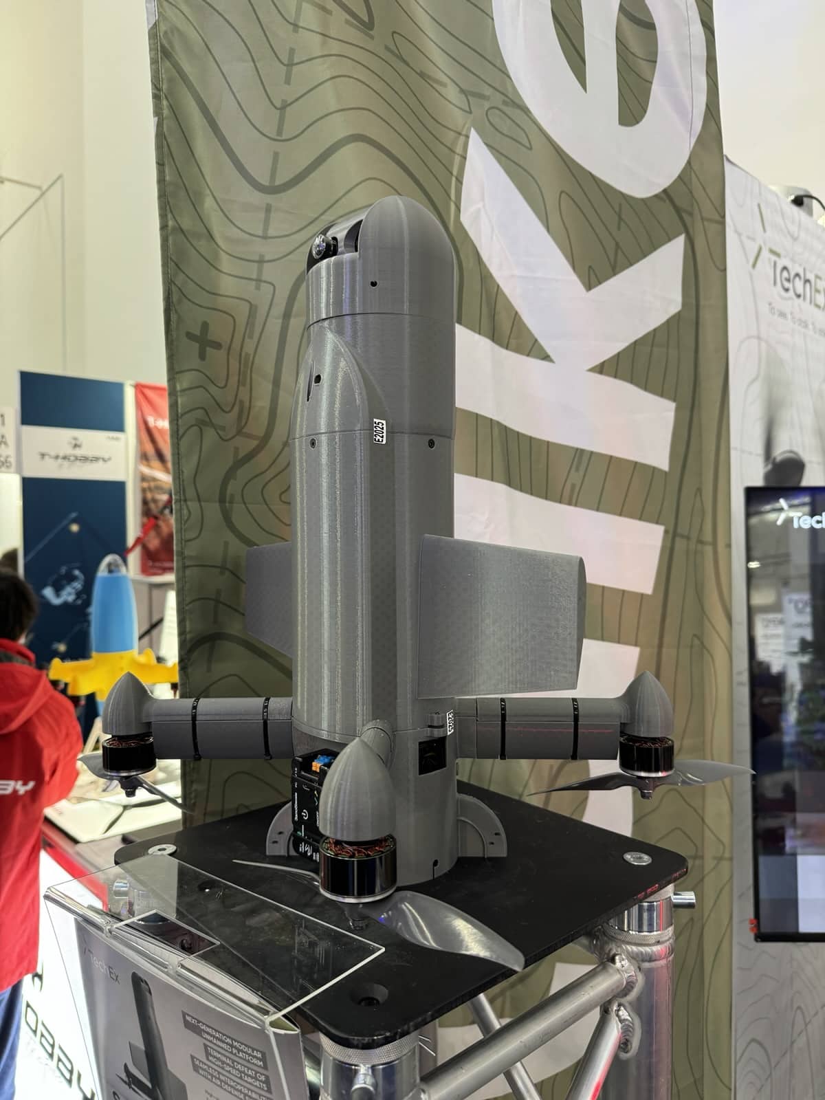 Grey modular strike drone displayed upright on a TechEx trade show stand.