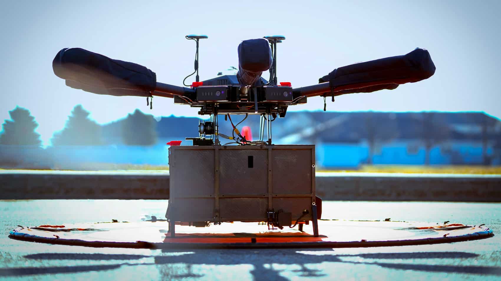 Flytrex delivery drone lifting a cardboard box from a painted landing pad.