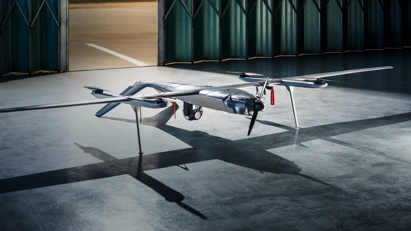 Tekever fixed-wing reconnaissance drone parked inside a dimly lit hangar.
